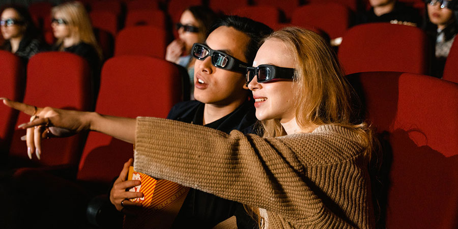 couple wearing 3D glasses while pointing and watching a movie inside a cinema