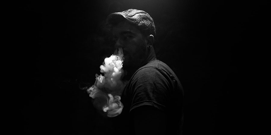man wearing black t-shirt exhaling smoke in the dark